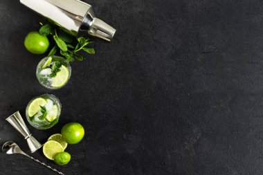 Buzlu mojito kokteyli yapmak için gereken malzemeler ve bardaklar, siyah arka planda taze nane ve limon. Mojito kokteyli yapmak için bar aksesuarları..