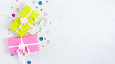 Beyaz ahşap arka planda fiyonklu renkli bir kağıda sarılı hediye kutuları. Parti geçmişi hediyeler ve konfetilerle dolu.