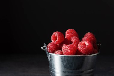 Siyah arka planda metal bir kovada taze olgun ahududular. Vitamin dolu sulu ahududu.