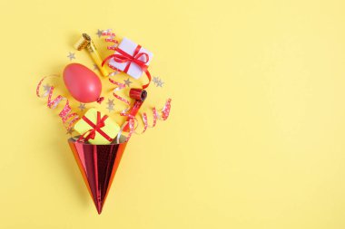 Doğum günü partisi dekorasyonlu doğum günü şapkası ve pastel sarı arka plan manzaralı hediyeler. Parti dekorasyonlu yaratıcı kompozisyon.