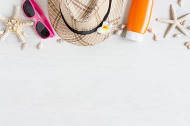 Beyaz ahşap güvertede plaj aksesuarları olan bir yaz. Pembe güneş gözlükleri, şapka, denizyıldızı ve ahşap arka planda güneş kremi..