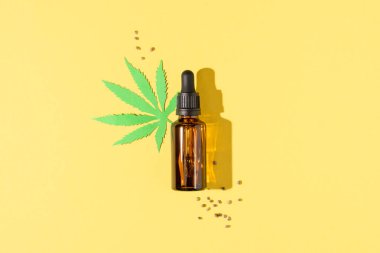 Kenevir yağı damlacık şişesinde ve tohumlar sarı arka planda. Tıbbi marihuana cbd yağı. Alternatif tıp, bitkisel doğal kenevir kozmetik.