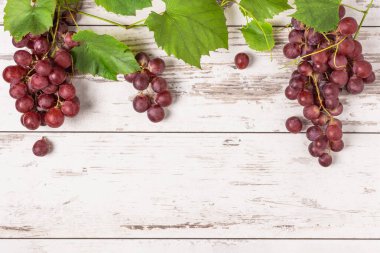 Beyaz ahşap arka planda yaprakları olan olgun kırmızı üzümler. Tasarım için kopyalama alanı olan üzüm meyvesi arkaplanı.