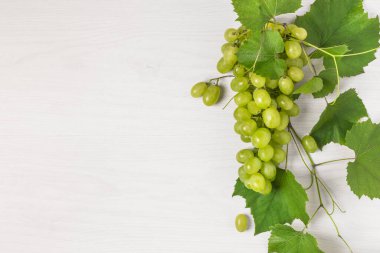 Beyaz ahşap arka planda yaprakları olan olgun yeşil üzümler. Tasarım için kopyalama alanı olan üzüm meyvesi arkaplanı.