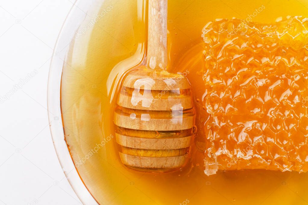 Healthy organic honey in a plate with honeycomb and wooden honey dipper top view on white background. Sweet honey healthy dessert.