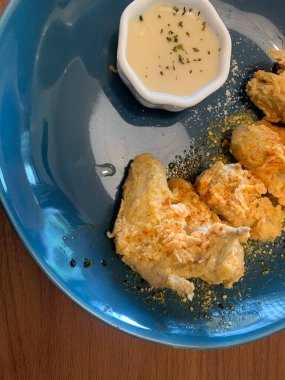 Ahşap masada mavi tabakta servis edilen kızarmış tavuk kanatları. Yanında da otlarla süslenmiş küçük bir tabak kremalı beyaz sos..