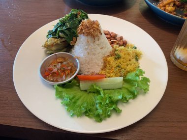 Bebek Betutu rostosu ördeği eşliğinde sunulan beyaz tabakta servis edilen bale yemeği ve üzerine kızarmış arpacık soğanı ile bol miktarda pirinç. Sotelenmiş sebzeler rendelenmiş hindistan cevizi, kızarmış fıstık, salata, marul, salatalık, domates dilimi içerir..