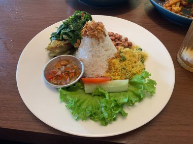 Bebek Betutu rostosu ördeği eşliğinde sunulan beyaz tabakta servis edilen bale yemeği ve üzerine kızarmış arpacık soğanı ile bol miktarda pirinç. Sotelenmiş sebzeler rendelenmiş hindistan cevizi, kızarmış fıstık, salata, marul, salatalık, domates dilimi içerir..