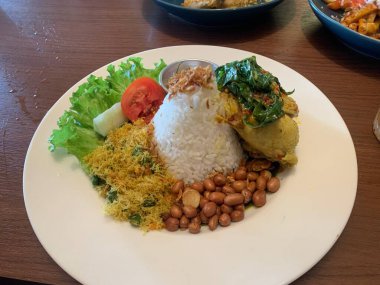 Bebek Betutu rostosu ördeği eşliğinde sunulan beyaz tabakta servis edilen bale yemeği ve üzerine kızarmış arpacık soğanı ile bol miktarda pirinç. Sotelenmiş sebzeler rendelenmiş hindistan cevizi, kızarmış fıstık, salata, marul, salatalık, domates dilimi içerir..