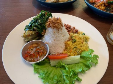 Bebek Betutu rostosu ördeği eşliğinde sunulan beyaz tabakta servis edilen bale yemeği ve üzerine kızarmış arpacık soğanı ile bol miktarda pirinç. Sotelenmiş sebzeler rendelenmiş hindistan cevizi, kızarmış fıstık, salata, marul, salatalık, domates dilimi içerir..