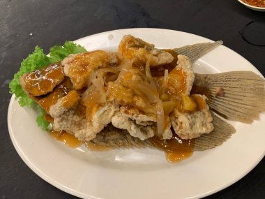 Domates, marul, dolmalık biber, sarımsak ve beyaz tabakta Tamarind soslu acılı gourami balığı. Tayland geleneksel yemek tarzı..