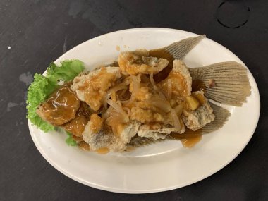 Domates, marul, dolmalık biber, sarımsak ve beyaz tabakta Tamarind soslu acılı gourami balığı. Tayland geleneksel yemek tarzı..