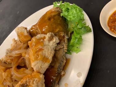 Domates, marul, dolmalık biber, sarımsak ve beyaz tabakta Tamarind soslu acılı gourami balığı. Tayland geleneksel yemek tarzı..