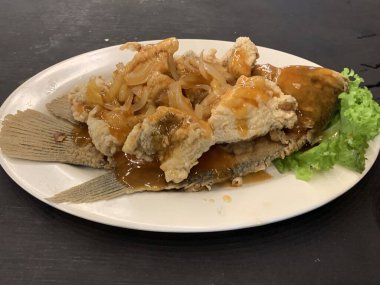 Domates, marul, dolmalık biber, sarımsak ve beyaz tabakta Tamarind soslu acılı gourami balığı. Tayland geleneksel yemek tarzı..