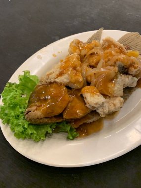 Domates, marul, dolmalık biber, sarımsak ve beyaz tabakta Tamarind soslu acılı gourami balığı. Tayland geleneksel yemek tarzı..