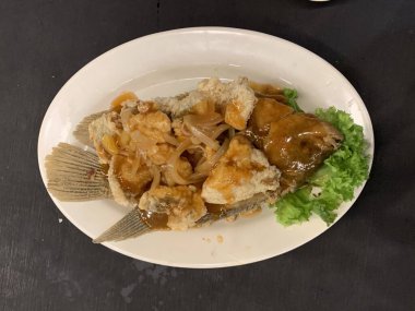 Domates, marul, dolmalık biber, sarımsak ve beyaz tabakta Tamarind soslu acılı gourami balığı. Tayland geleneksel yemek tarzı..