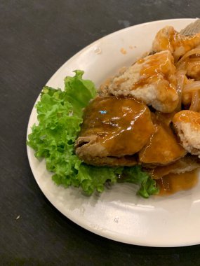 Domates, marul, dolmalık biber, sarımsak ve beyaz tabakta Tamarind soslu acılı gourami balığı. Tayland geleneksel yemek tarzı..