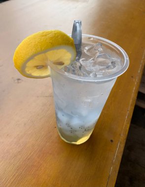 Bir bardak buzlu soda ve üstüne bir dilim limon. Tahta masanın üzerine serinletici bir dokunuş ekleyin. Tropik içki konsepti.