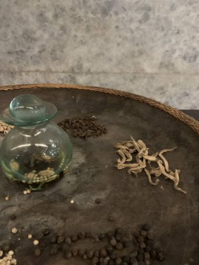 Yuvarlak tepside çeşitli doğal eşyalar sergilenir. Görünür elementler arasında tarçın çubukları, yıldız anason, aroma terapisi gibi küçük şeffaf cam bir kap bulunur. Bu düzenleme büyük ihtimalle ritüellere hizmet ediyor..