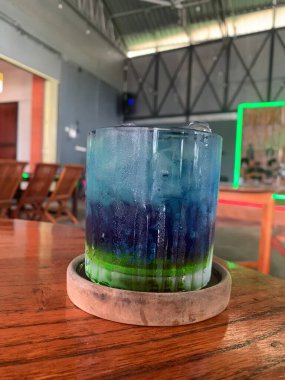 Kurumuş narenciye garnitürlü dokuma bardakta servis edilen canlı mavi kokteyl. İçki ferahlatıcı gibi görünüyor, muhtemelen alkolsüz moktail içeriyor limonata gibi..