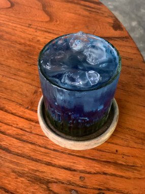 Kurumuş narenciye garnitürlü dokuma bardakta servis edilen canlı mavi kokteyl. İçki ferahlatıcı gibi görünüyor, muhtemelen alkolsüz moktail içeriyor limonata gibi..