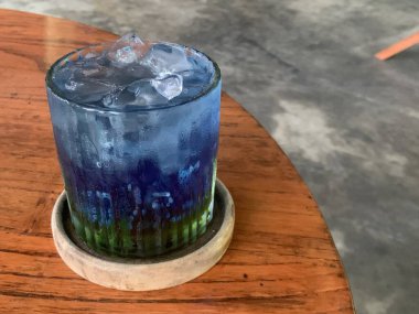 Kurumuş narenciye garnitürlü dokuma bardakta servis edilen canlı mavi kokteyl. İçki ferahlatıcı gibi görünüyor, muhtemelen alkolsüz moktail içeriyor limonata gibi..