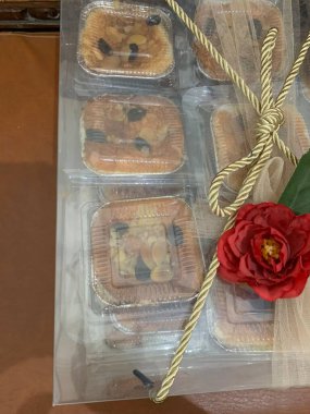 Temiz kutu, kırmızı yapay çiçek ve yeşil yapraklı dekoratif elementlerle süslenmiş birden fazla küçük pasta içeriyor. Bu da düğün hediyesi sunumunu öneriyor..