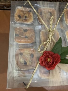 Temiz kutu, kırmızı yapay çiçek ve yeşil yapraklı dekoratif elementlerle süslenmiş birden fazla küçük pasta içeriyor. Bu da düğün hediyesi sunumunu öneriyor..