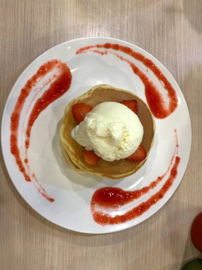 Üstü vanilyalı dondurma, çırpılmış çırpılmış ve beyaz tabağa konmuş meyve dilimleri ile kaplanmış çilekli krep. Tatlı sos ahşap masada servis edilen tabağın kenarlarında süslenmiş..