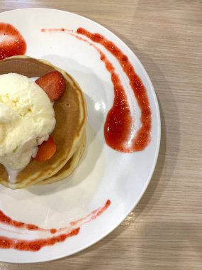 Üstü vanilyalı dondurma, çırpılmış çırpılmış ve beyaz tabağa konmuş meyve dilimleri ile kaplanmış çilekli krep. Tatlı sos ahşap masada servis edilen tabağın kenarlarında süslenmiş..
