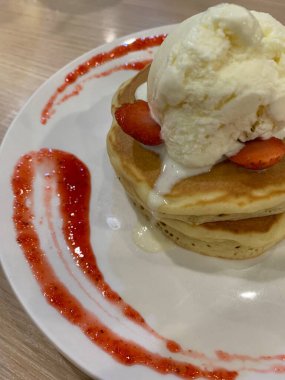 Üstü vanilyalı dondurma, çırpılmış çırpılmış ve beyaz tabağa konmuş meyve dilimleri ile kaplanmış çilekli krep. Tatlı sos ahşap masada servis edilen tabağın kenarlarında süslenmiş..