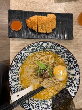 Dilimlenmiş yeşil soğan ve mantarla kaplı erişte ve katsuyla dolu dekoratif bir kase. Et suyu bol kremalı, görünür yağ damlacıkları gibi görünüyor.