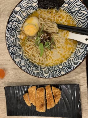 Dilimlenmiş yeşil soğan ve mantarla kaplı erişte ve katsuyla dolu dekoratif bir kase. Et suyu bol kremalı, görünür yağ damlacıkları gibi görünüyor.