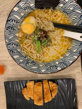 Dilimlenmiş yeşil soğan ve mantarla kaplı erişte ve katsuyla dolu dekoratif bir kase. Et suyu bol kremalı, görünür yağ damlacıkları gibi görünüyor.