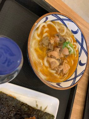 Dilimlenmiş yeşil soğan ve mantarla kaplı erişte ve katsuyla dolu dekoratif bir kase. Et suyu bol kremalı, görünür yağ damlacıkları gibi görünüyor.