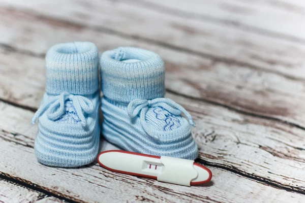 Young woman holding baby shoes and positive pregnancy test — Stock Photo, Image