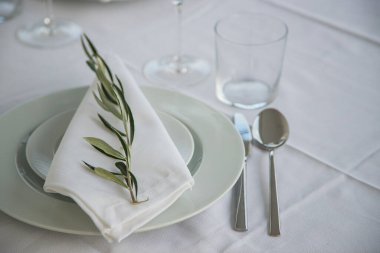 Beyaz tabaklar, cam eşyalar ve her peçetede basit bir zeytin dalı olan iki kişilik şık bir açık hava masası. Yaşam tarzına, minimalizme ve detaylara odaklan..