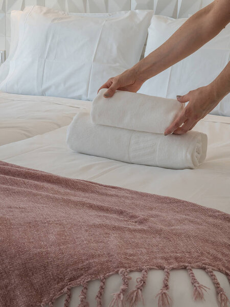 Detail of a person carefully arranging soft white towels on a modern bed, illustrating comfort, care, and hospitality in a welcoming, peaceful, and well-designed home or guest accommodation.