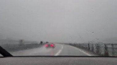 Şiddetli yağmurda otoyolda araba süren bir araç, görüş mesafesi ve tehlikeli yol koşullarıyla mücadele ediyor. Aktif silecekler ve bulanık ışıklar, şiddetli hava koşullarında seyahat riskini vurgular.