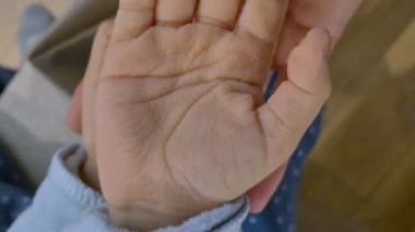 Bir çocuk iki avucunu da tutar, uzun süre suda kaldıktan sonra derisi buruşur, yetişkin bir el ise nazikçe onları destekler. Yakın çekim, evdeki aile bakımını, dokunuşunu ve çocukluk anılarını vurguluyor.