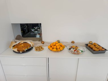 Beyaz büfe, yılbaşı tatlı tezgahı olarak düzenlenir. Sünger keki, geleneksel kral pastası, Fransız tostu dilimleri, kurutulmuş incirler ve taze mandalinalar. Misafirleri renkli, tatlı bir ev seçiminin tadını çıkarmaya davet eder..