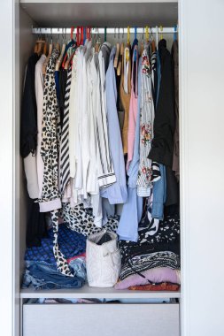 Dolabın parmaklıklarında desenli gömlekler, bluzlar ve montlarla karışık askılarda asılı günlük kıyafet deposu ve yatak odasındaki gerçek ev düzenini gösteriyor..