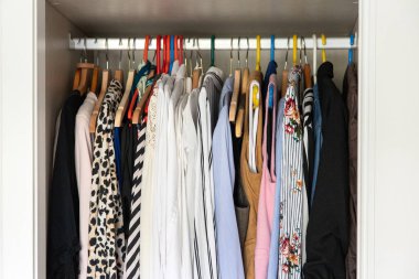 Dolabın parmaklıklarında desenli gömlekler, bluzlar ve montlarla karışık askılarda asılı günlük kıyafet deposu ve yatak odasındaki gerçek ev düzenini gösteriyor..