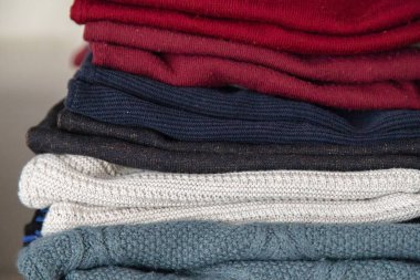 Bir rafa düzgünce dizilmiş katlanmış örgü süveter yığını, rahat dokuları vurgulamak ve evdeki kışlık giysiler için düzenlenmiş gardırop deposu.