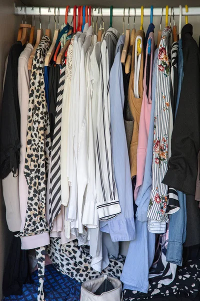 Dolabın parmaklıklarında desenli gömlekler, bluzlar ve montlarla karışık askılarda asılı günlük kıyafet deposu ve yatak odasındaki gerçek ev düzenini gösteriyor..