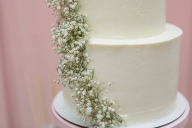 Zarif bir parti, düğün, vaftiz ya da doğum günü etkinliği için hazır, yumuşak pembe arka planda duran taze bebek nefesli çiçeklerle süslenmiş minimal beyaz kutlama pastası..