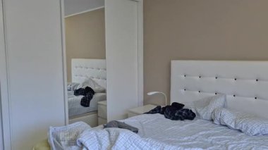 Gerçek bir yatak odasında kırışık çarşaflar ve kıyafetlerle dağınık, dağınık, dağınık bir ev ortamını ve günlük yaşantısını gösteren çift kişilik bir yatak..