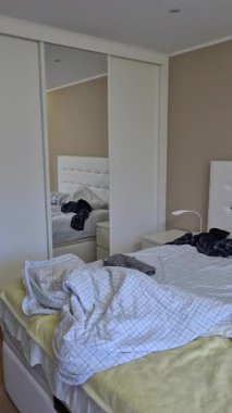 Gerçek bir yatak odasında kırışık çarşaflar ve kıyafetlerle dağınık, dağınık, dağınık bir ev ortamını ve günlük yaşantısını gösteren çift kişilik bir yatak..