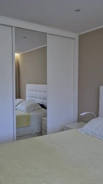 Parlak bir ev yatak odasında, yastıklı beyaz yatak başlığı, yumuşak yatak başlığı ve komodiniyle temiz bir iç mekan, konfor ve günlük organizasyonun göstergesi olarak çift kişilik yatak yapıldı..