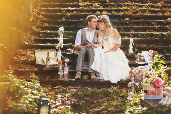 Les mariés dans le style rétro étreignant sur les marches de pierre à la forêt d'automne, entouré par le décor de mariage . — Photo